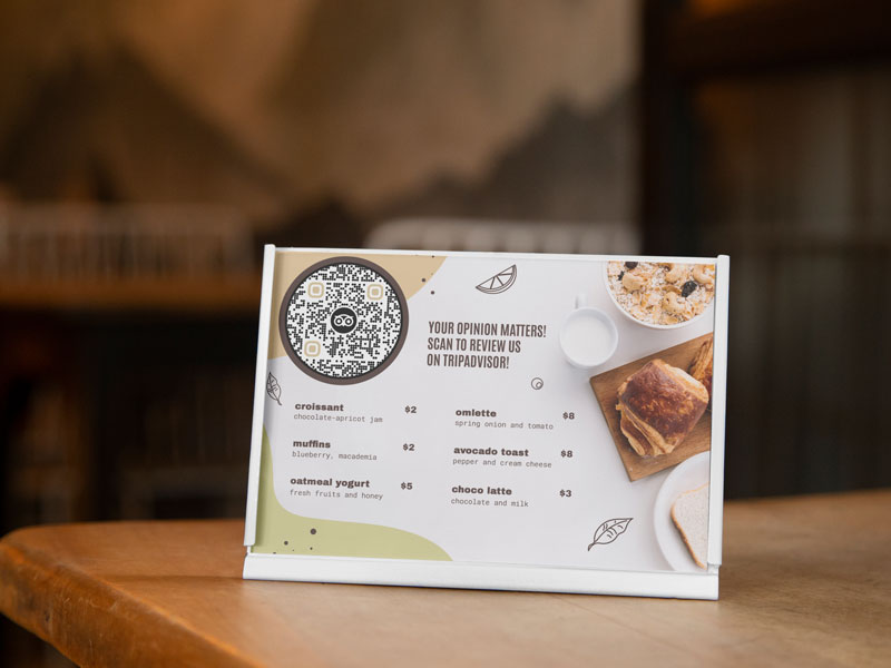 Código QR de Tripadvisor en la mesa de una cafetería con clientes escribiendo reseñas